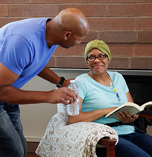 Man bringing bottle of water to woman sitting in chair.