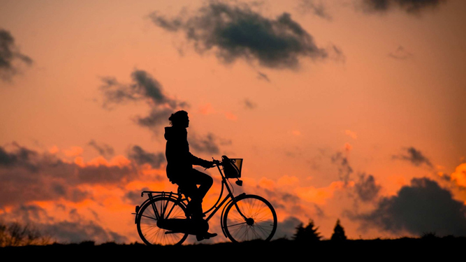 image of woman cycling in front of sunset